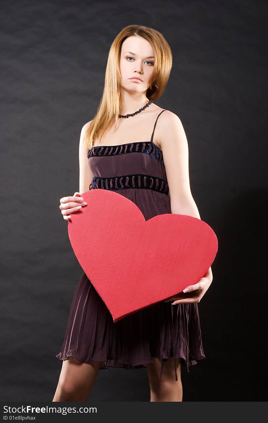 Girl in dress holding red heart  over black background