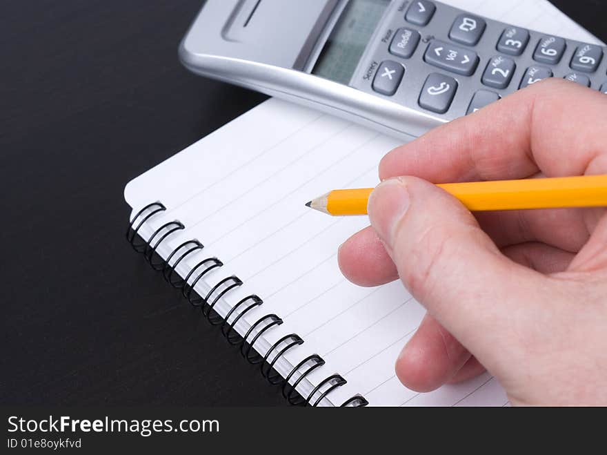 Yellow pencil writing in a blank spiral-bound notebook on which sits a telephone. Yellow pencil writing in a blank spiral-bound notebook on which sits a telephone.