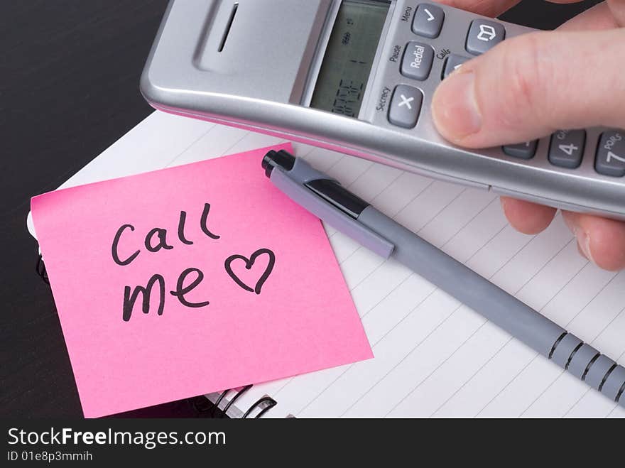 Phone on a spiral notebook with pink postit note saying CALL ME. Heart on postit. Concept for office romance or lifestyle. Phone on a spiral notebook with pink postit note saying CALL ME. Heart on postit. Concept for office romance or lifestyle.