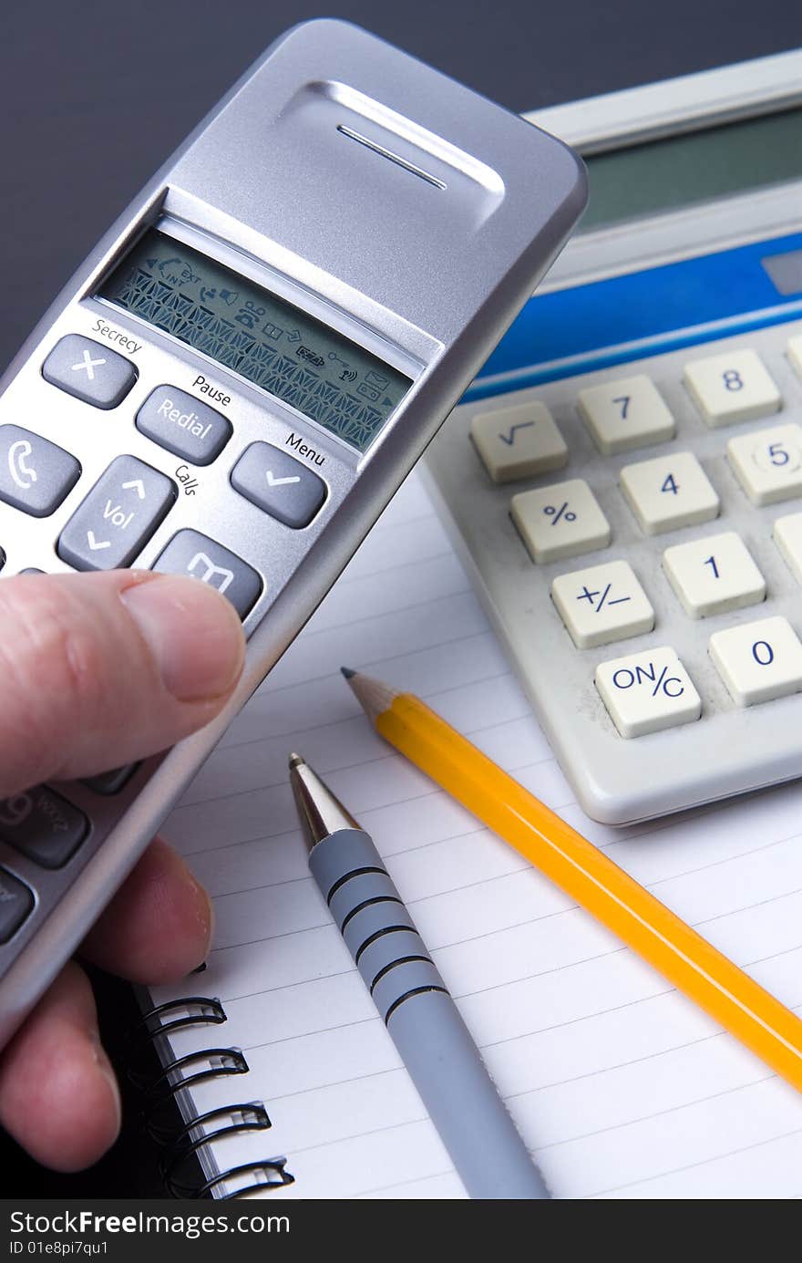 Phone and calculator on a spiral notebook with pen and pencil. Differential focus.