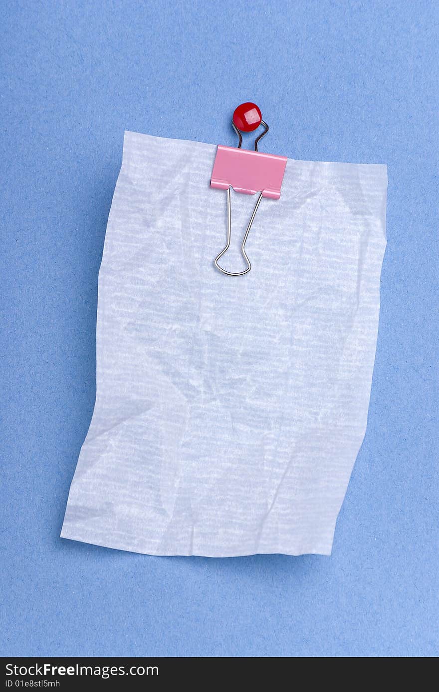 Blank notepaper on blue background crushed and hung from clip held by red drawing pin.