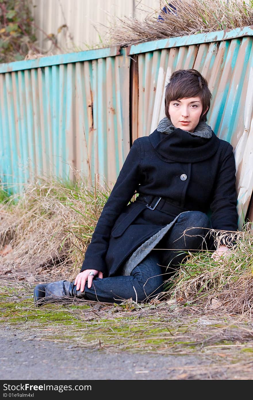 A fashion model sits in some grass next to an old rusty wall. A fashion model sits in some grass next to an old rusty wall.