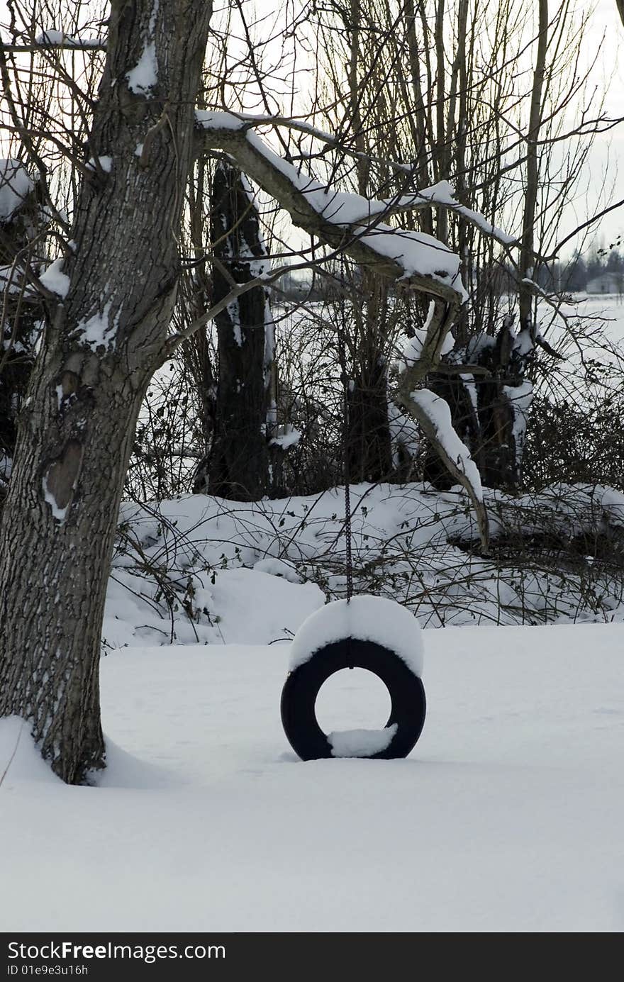 A snow covered tire swing alone on a cold winter day in a rural country yard. A snow covered tire swing alone on a cold winter day in a rural country yard.