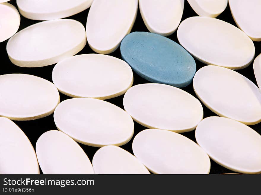 Macro shot of white pills with one blue pill.