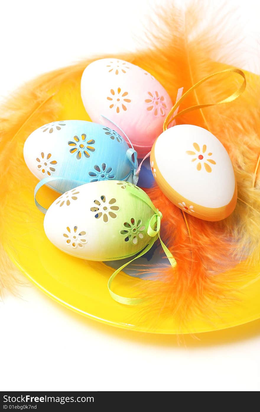 Easter eggs on yellow plate with yellow and orange feathers.