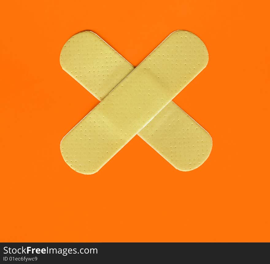 Two plasters forming a cross on orange background