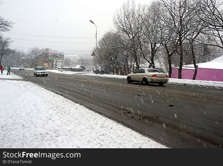 Motor vehicles go on slippery dangerous road on background of the snowfall