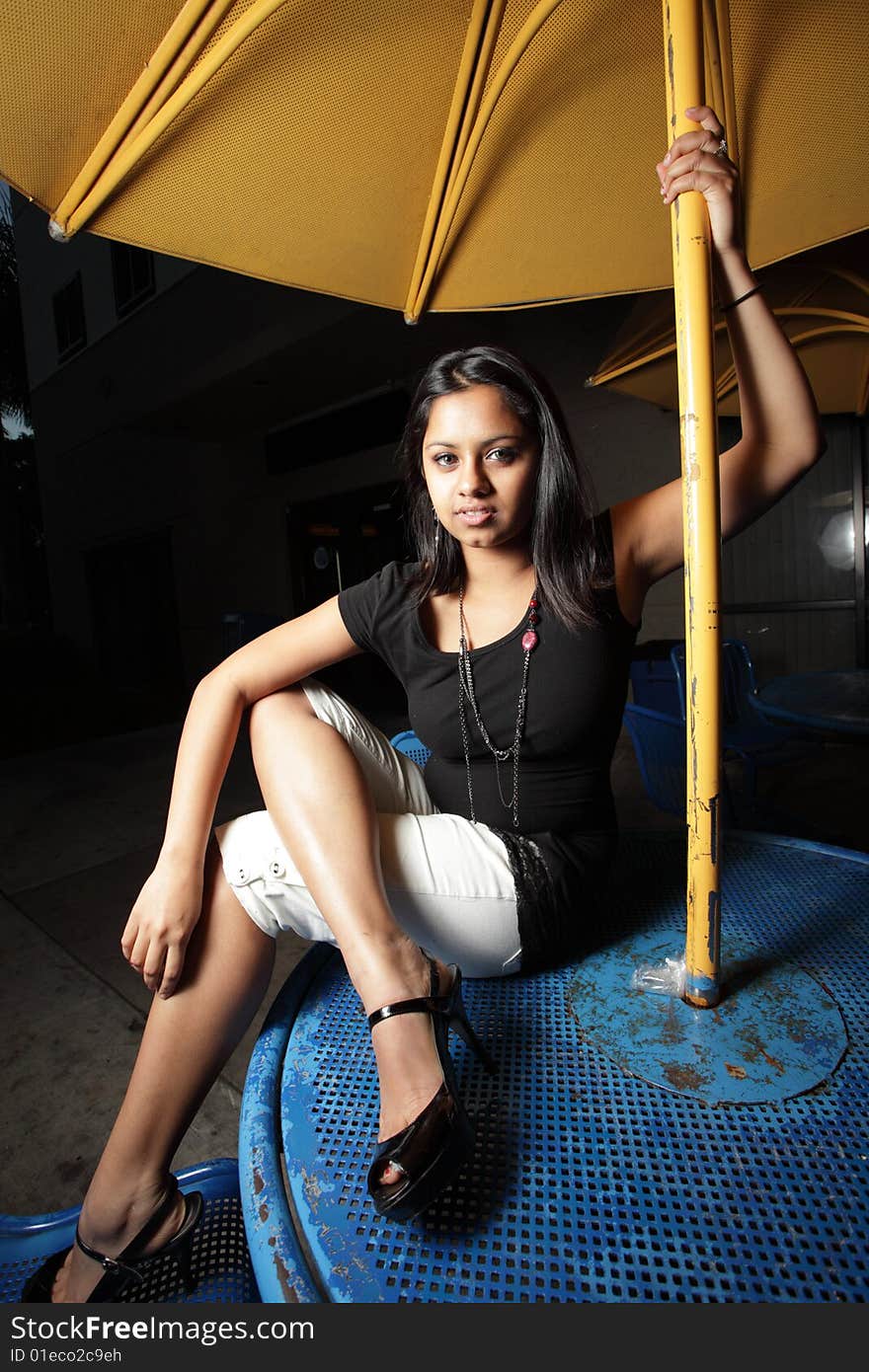 Young woman sitting on a blue table with a yellow metal table umbrella. Young woman sitting on a blue table with a yellow metal table umbrella