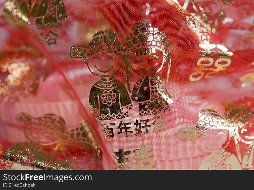 Thin translucent red meshed cloth decorated with gold Chinese characters and figures depicting marriage veiling a pair of heart shaped boxes with ribbons