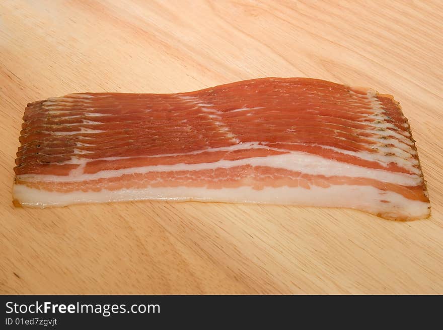 Raw bacon slices on wooden table.