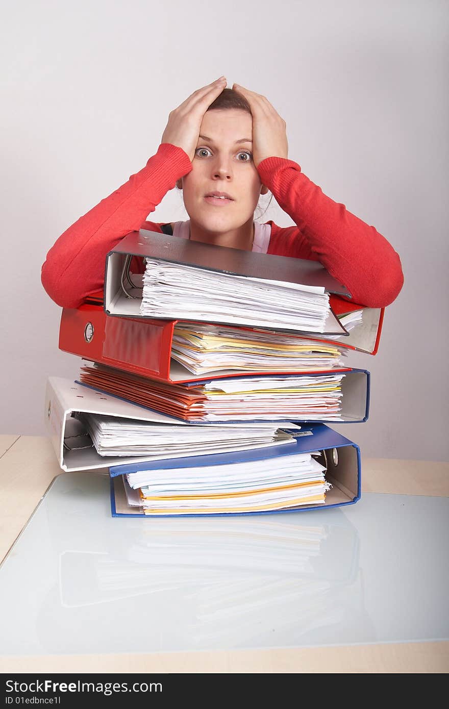 A young and beautiful female worker is stressed with a lot of paperwork in front of her. A lot of copyspace.