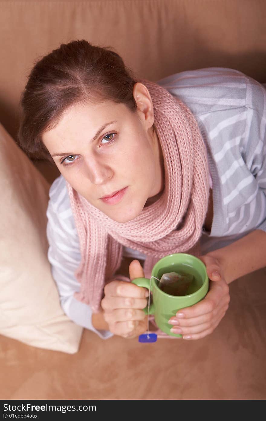 A young woman is sick. She is lying on the couch and is sneezing. She has a tea in her hand. A young woman is sick. She is lying on the couch and is sneezing. She has a tea in her hand.