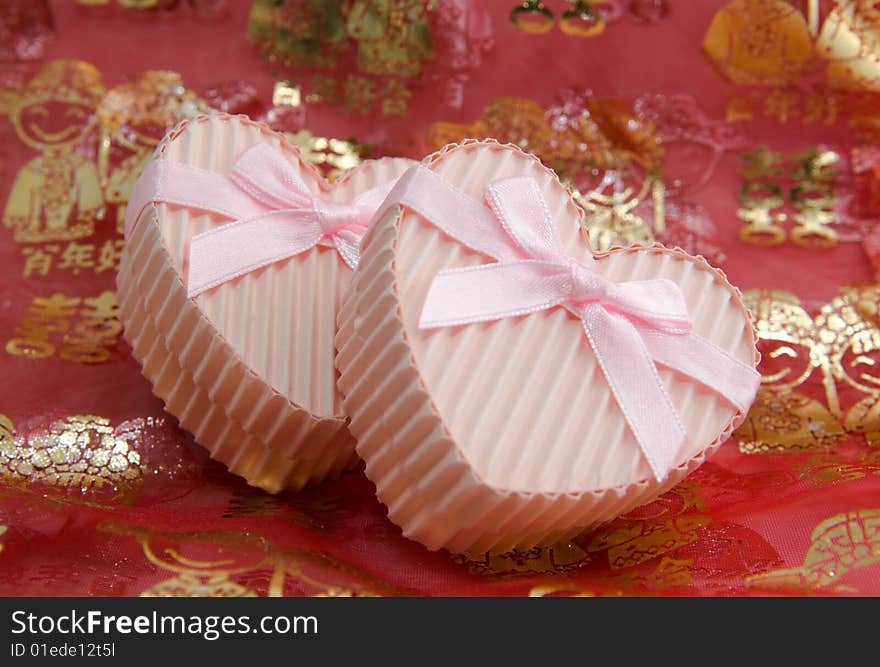 Still life of a pair of heart shaped boxes with ribbons on a red thin cloth decorated with gold Chinese characters and figures depicting marriage. Still life of a pair of heart shaped boxes with ribbons on a red thin cloth decorated with gold Chinese characters and figures depicting marriage