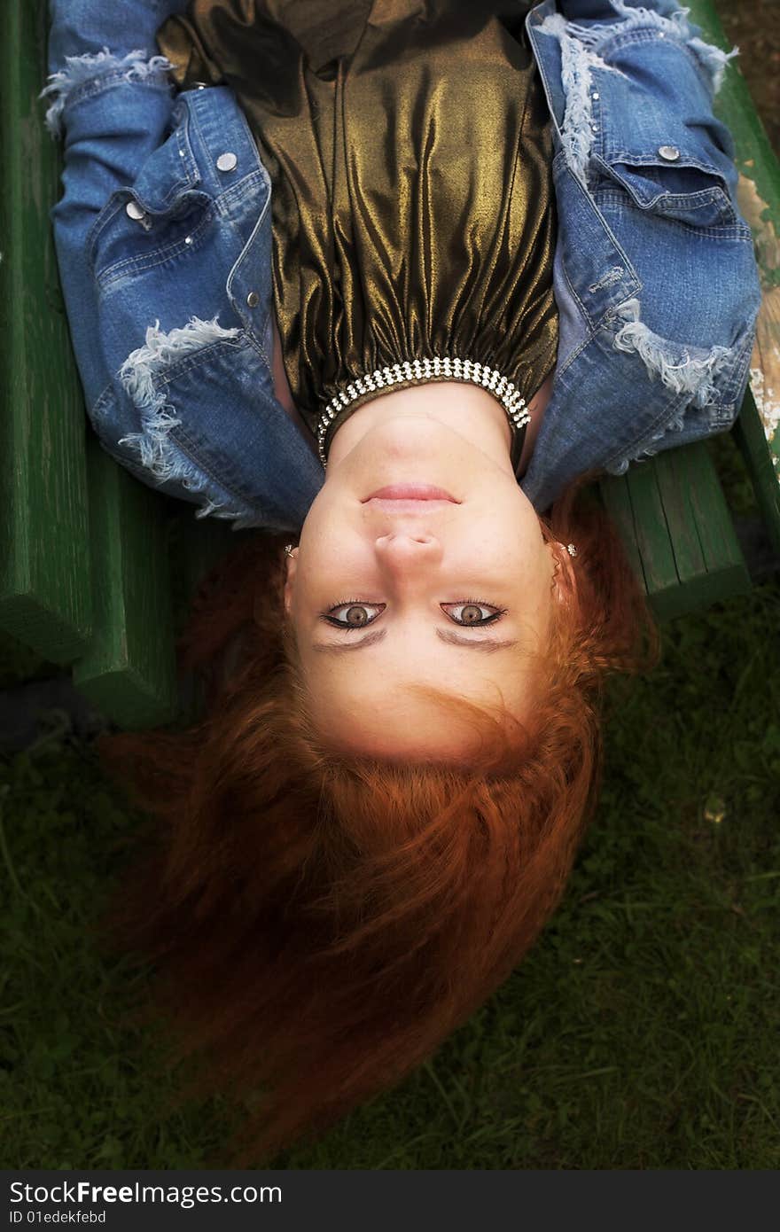 Portrait of a red-haired young woman relaxing on the bench in city-park