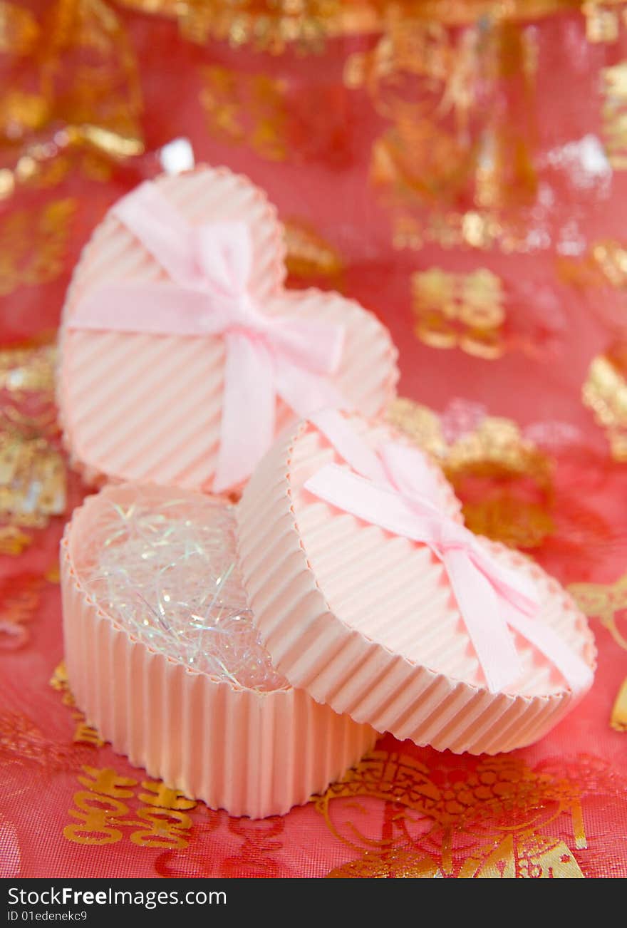 Still life of a pair of heart shaped boxes with ribbons on a red thin cloth decorated with gold Chinese characters and figures depicting marriage. Still life of a pair of heart shaped boxes with ribbons on a red thin cloth decorated with gold Chinese characters and figures depicting marriage