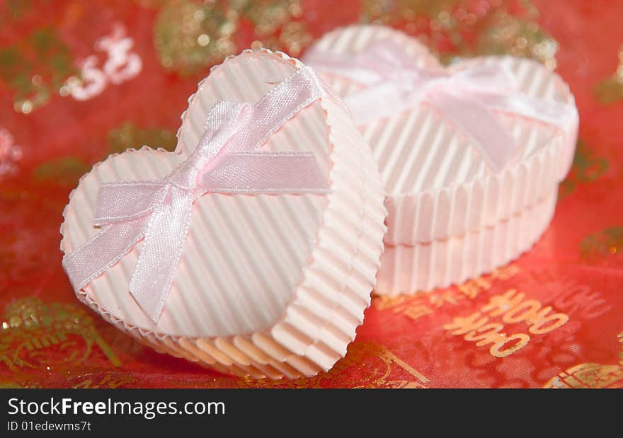 Still life of a pair of heart shaped boxes with ribbons on a red thin cloth decorated with gold Chinese characters and figures depicting marriage. Still life of a pair of heart shaped boxes with ribbons on a red thin cloth decorated with gold Chinese characters and figures depicting marriage