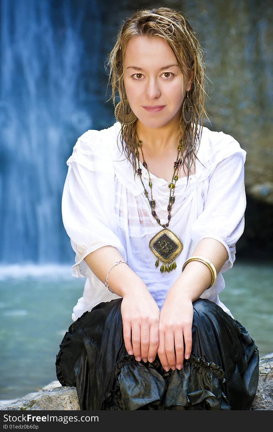 Young woman smiling at camera with blue waterfall as background. Young woman smiling at camera with blue waterfall as background