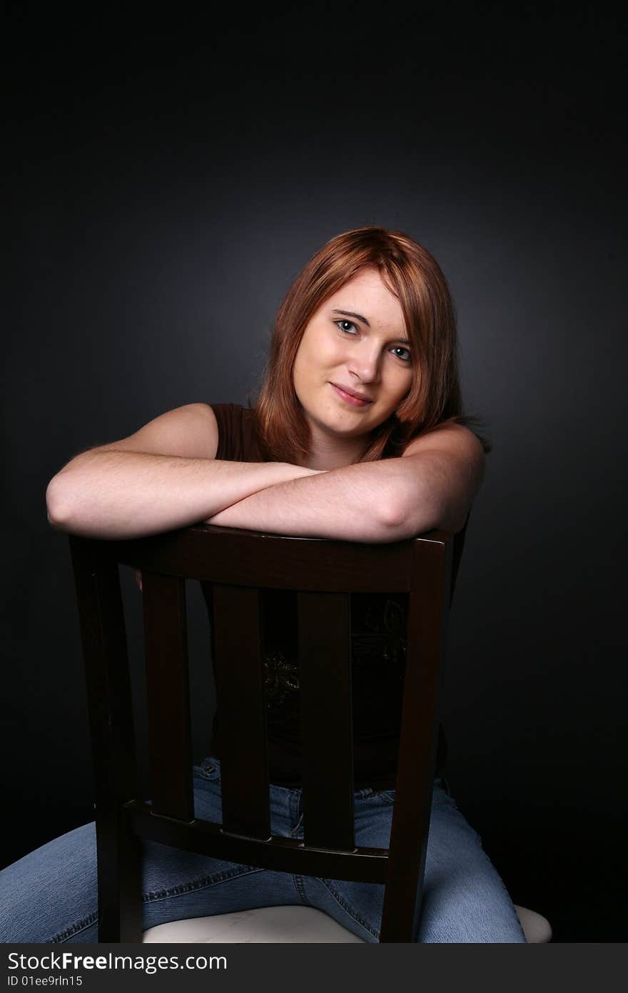 Pretty teenage girl with red hair with arms crossed on the back of a chair