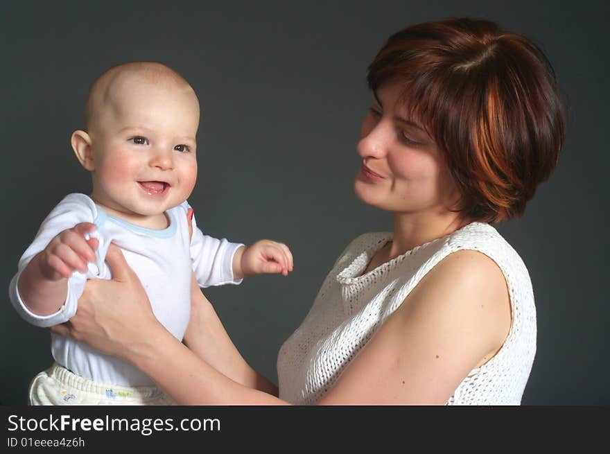 Laughing baby boy and his mother on grey background