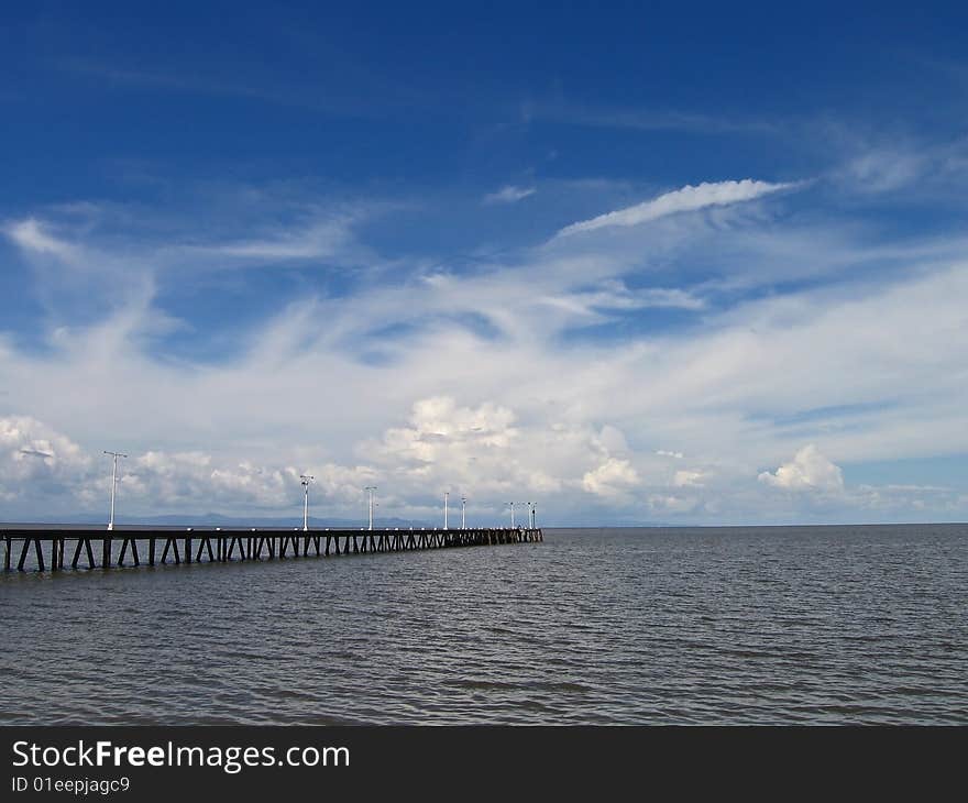 A long wooden dock on a lake with blue cloudy sky. A long wooden dock on a lake with blue cloudy sky