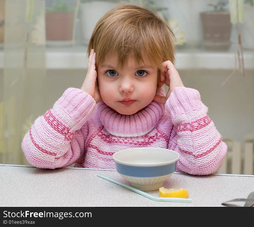 The little girl sits before a cup and drinks tea