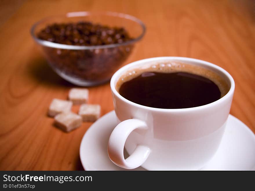 Cup of coffee, sugar and beans in glass bowl on wooden table