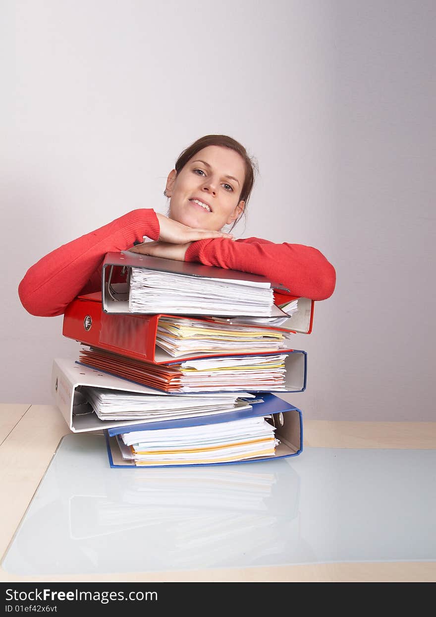 A young and beautiful female worker is smiling over a lot of paperwork in front of her. A lot of copyspace. A young and beautiful female worker is smiling over a lot of paperwork in front of her. A lot of copyspace.