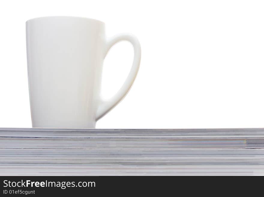 White cup on the heap of magazines isolated on white. White cup on the heap of magazines isolated on white.