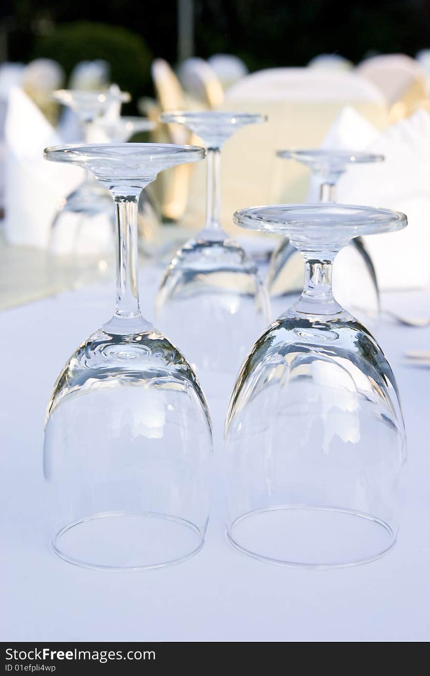 Two glasses upside down on a table. In the background and out of focus are more glasses and party tables decorated in white, gold and yellow.