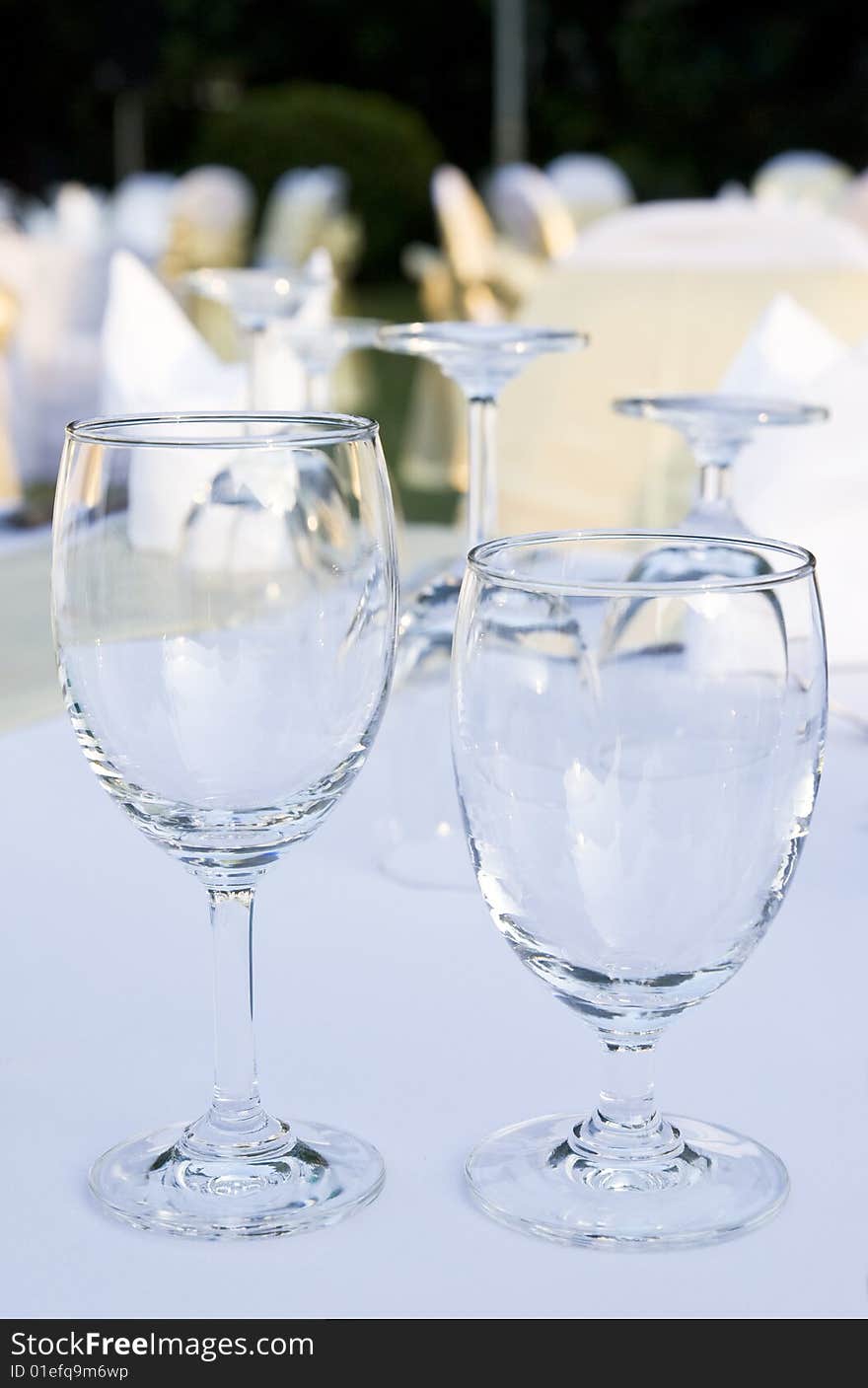 Two glasses on a table. In the background and out of focus are more glasses and party tables decorated in white, gold and yellow.