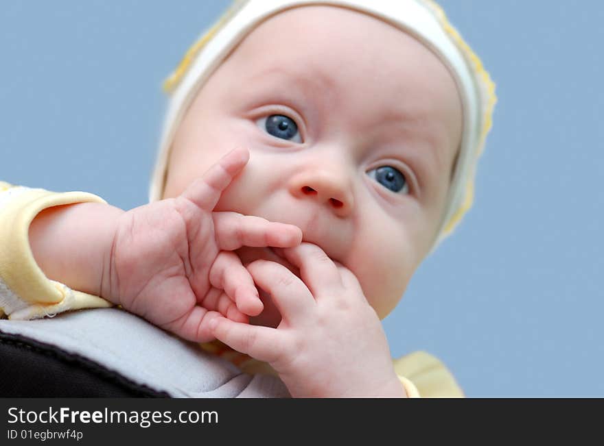 Little newbord boy with fingers in his mouth on blue background