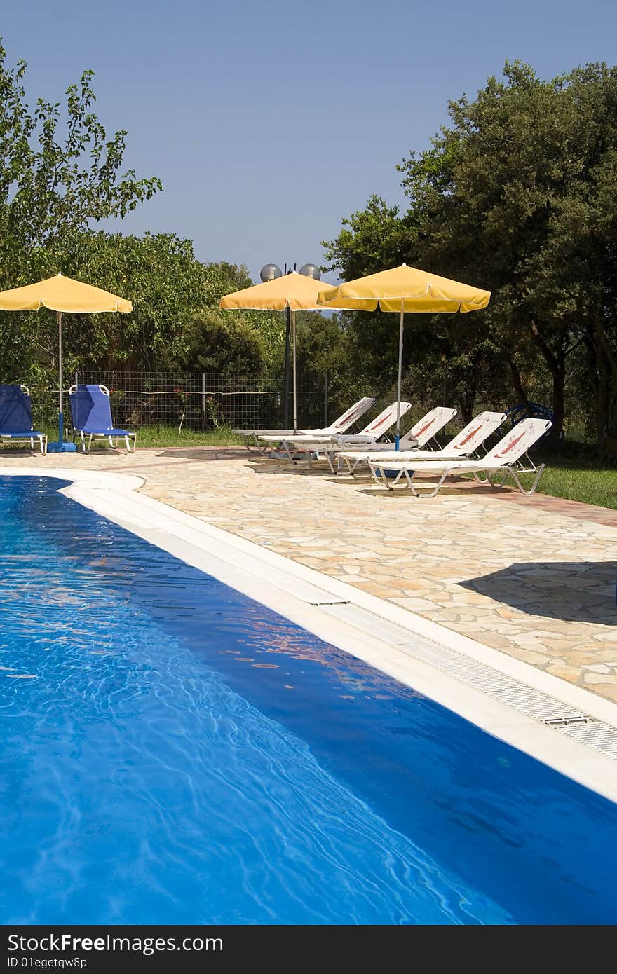 Sun loungers by a deep blue swimming pool. Sun loungers by a deep blue swimming pool