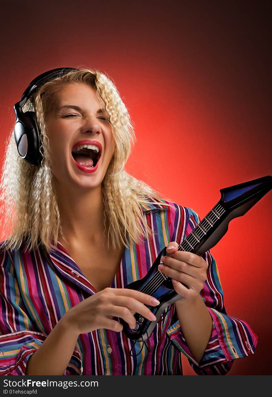 Beautiful young woman with headphones playing small electro guitar