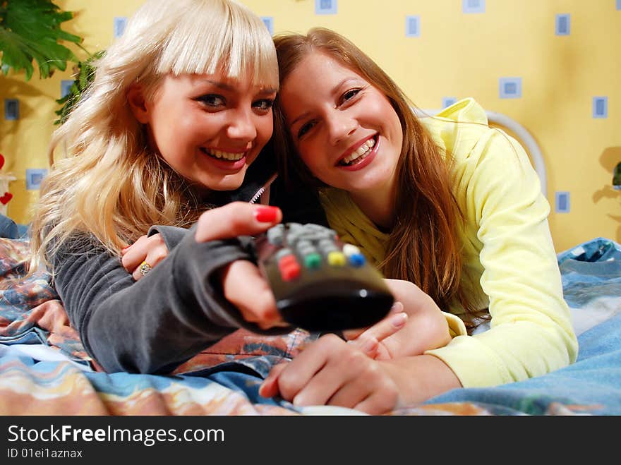 Two beautiful women watching television at the bedroom. Two beautiful women watching television at the bedroom