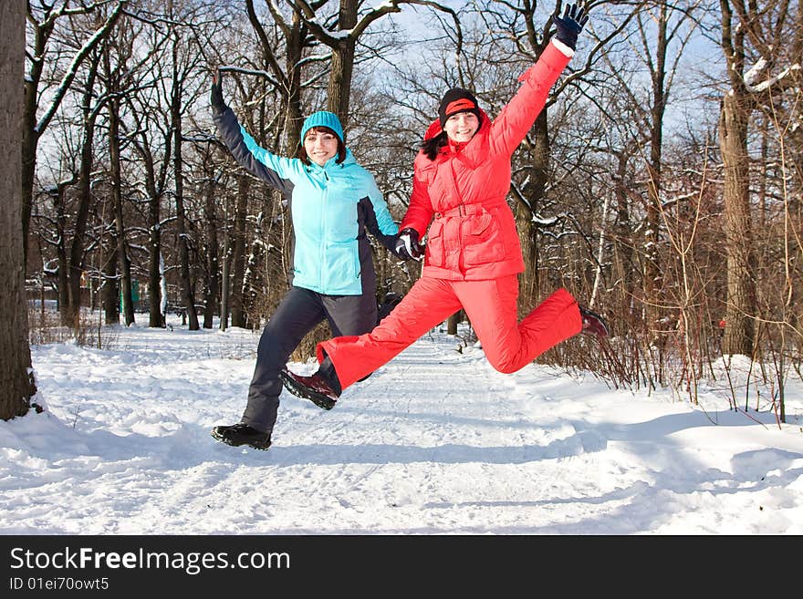 Two cheerful friendly girls jump in park