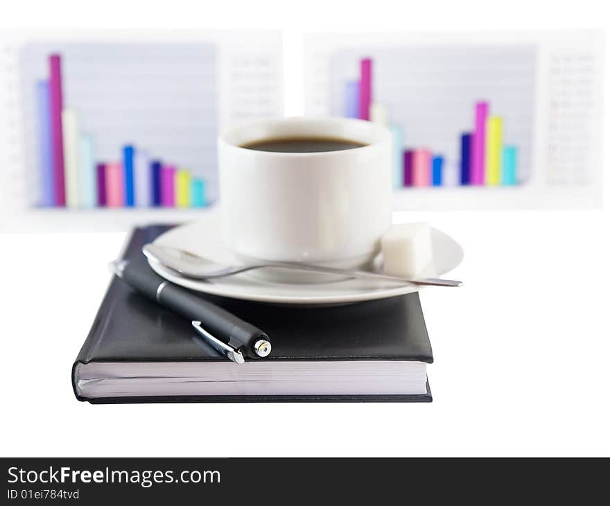 Coffee cup, standing on the black personal organizer, on a back background - two financial  diagrams . Focus at the pen. Isolated on white. Coffee cup, standing on the black personal organizer, on a back background - two financial  diagrams . Focus at the pen. Isolated on white.