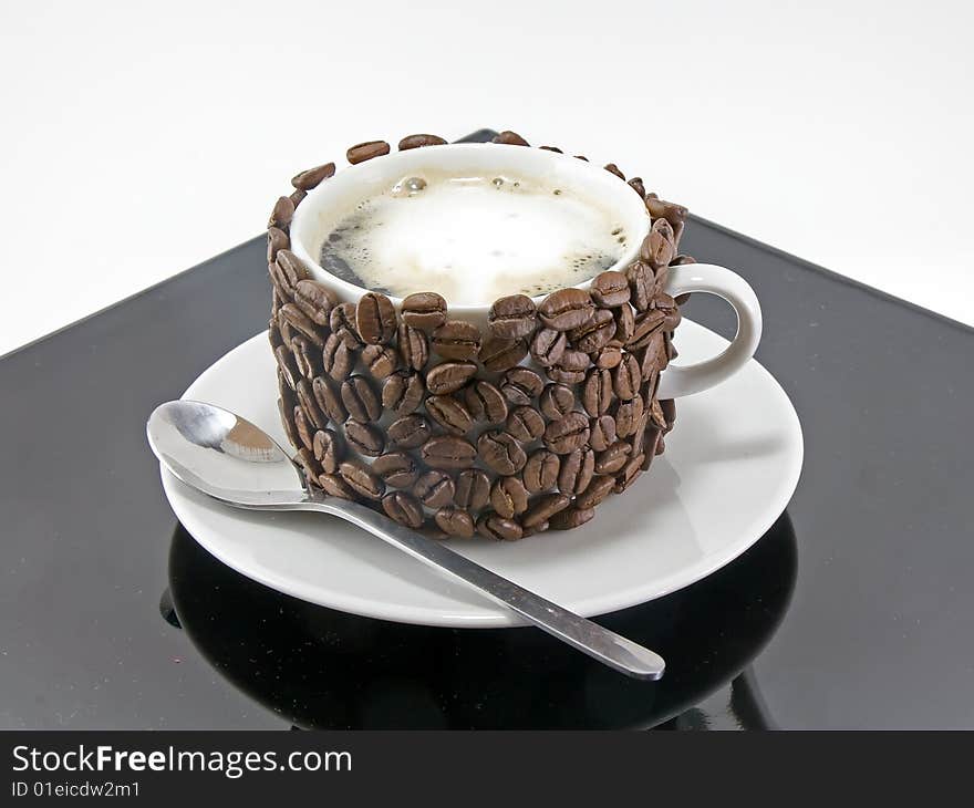 The coffee cup , original decorated by coffee grains(beans) on black plate. Isolated on white. The coffee cup , original decorated by coffee grains(beans) on black plate. Isolated on white.