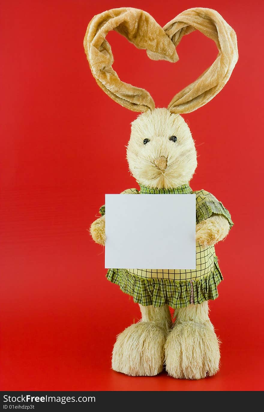 Straw hare with ears in the form of heart on a red background with the white nameplate. Straw hare with ears in the form of heart on a red background with the white nameplate.