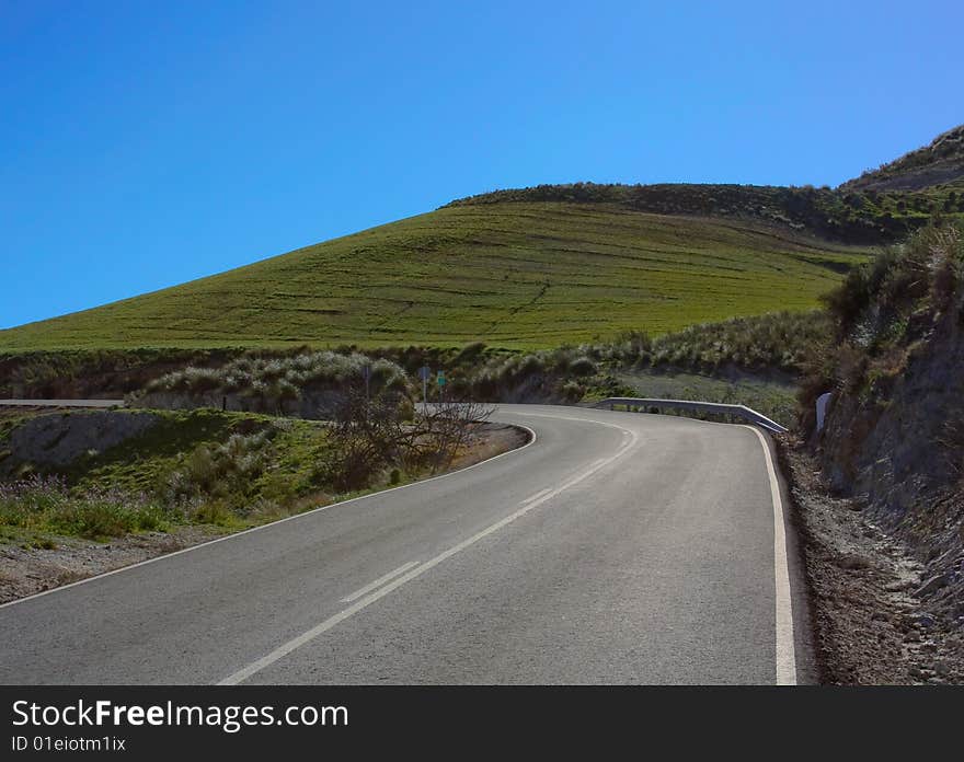 Road in early spring, green hill, blue sky