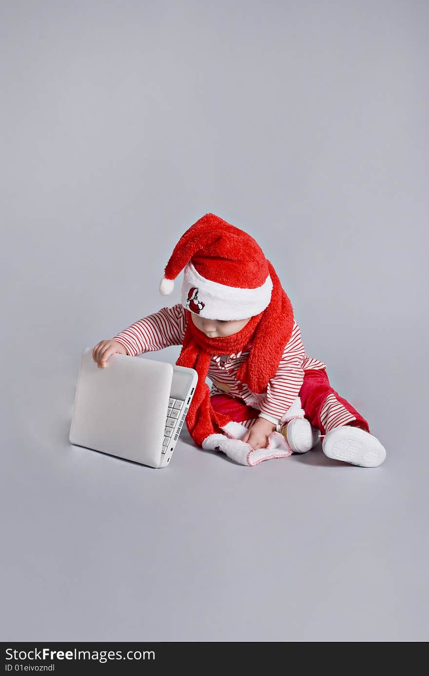 Baby santa claus with white laptop in grey background