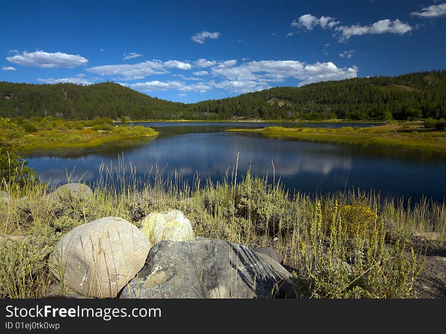 A refreshing lake with mountains covered in green pine trees in the background. A refreshing lake with mountains covered in green pine trees in the background