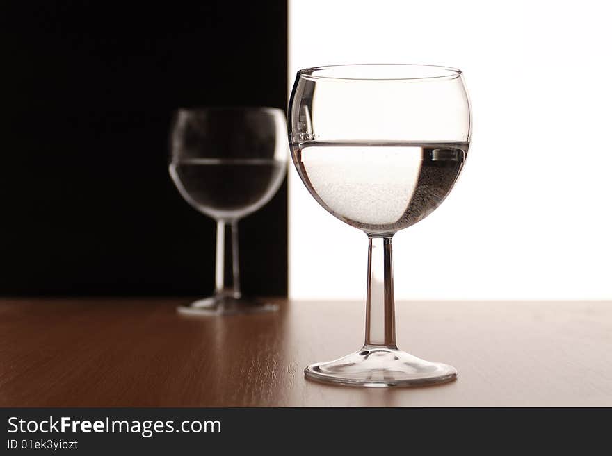 Two wine glasses in backlight on white and black contrast background