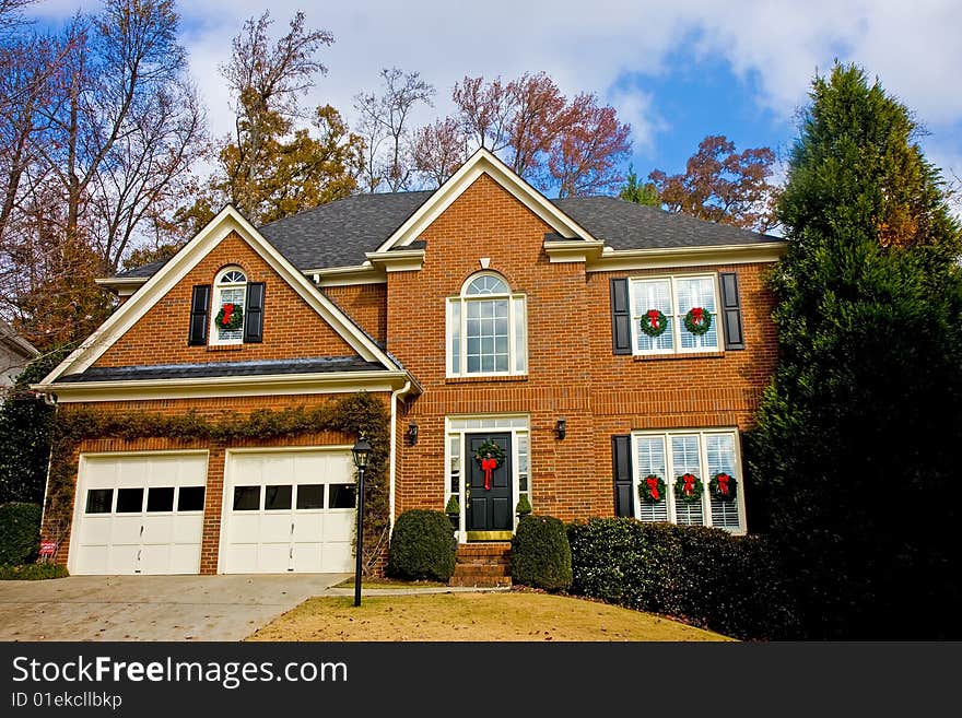 A nice brick house in a neighborhood with cloudy sky with Christmas wreaths. A nice brick house in a neighborhood with cloudy sky with Christmas wreaths