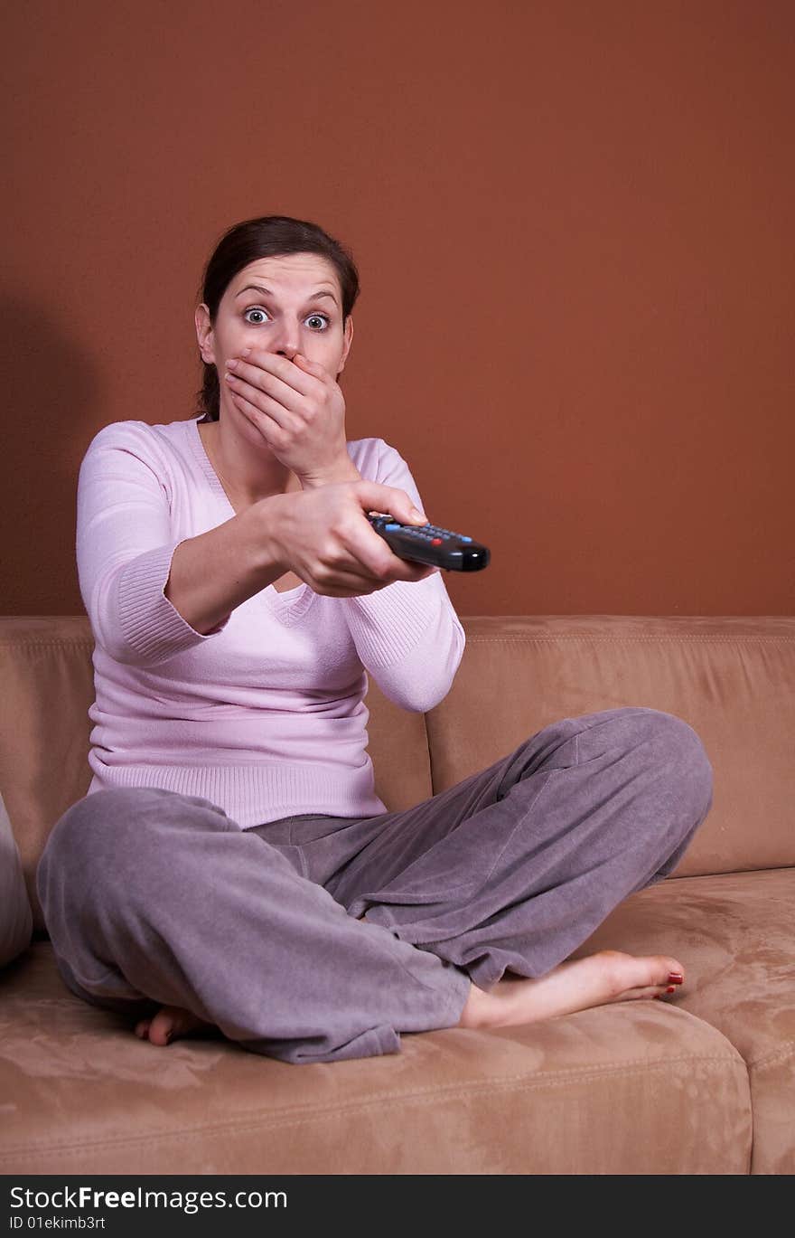 A young woman sits in front of a TV with the remote control in her hand on a couch. A lot of copyspace left. She seems to be afraid. A young woman sits in front of a TV with the remote control in her hand on a couch. A lot of copyspace left. She seems to be afraid.