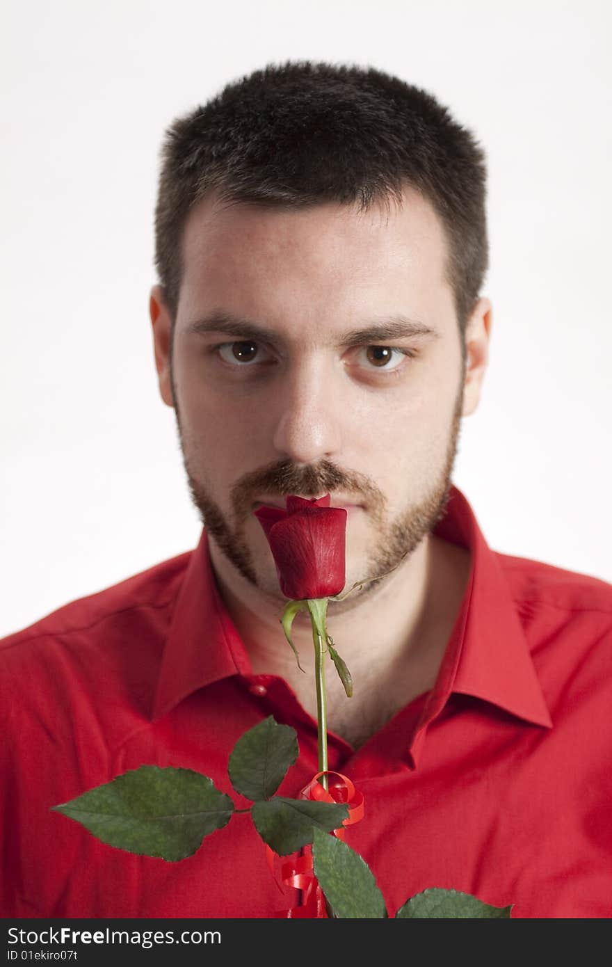 Young, handsome man in red shirt, holding a beautiful red rose in front of his mouth. Young, handsome man in red shirt, holding a beautiful red rose in front of his mouth