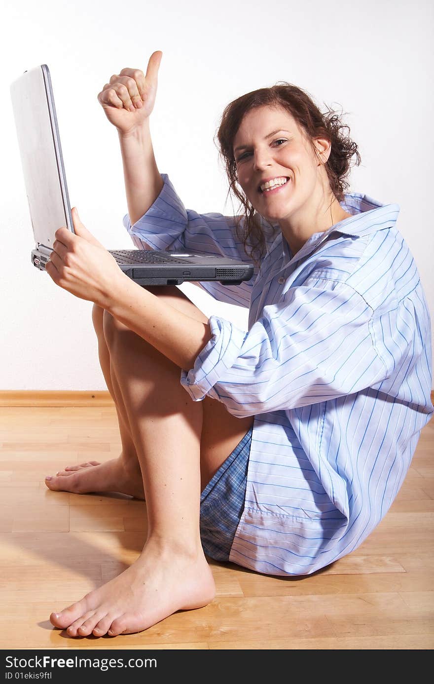 A young woman at home with her laptop sitting on the floor in her new appartment. She gives a thumb-up sign. A young woman at home with her laptop sitting on the floor in her new appartment. She gives a thumb-up sign.