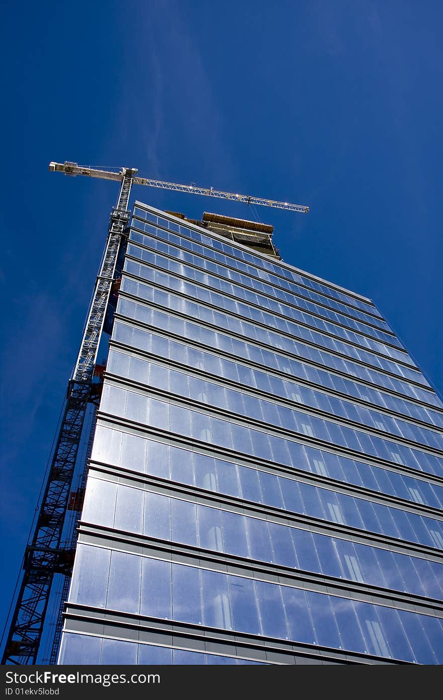 A blue glass high rise tower with a white crane on a bright blue sky. A blue glass high rise tower with a white crane on a bright blue sky