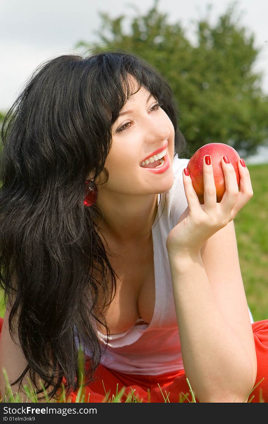 Pretty woman eating red apple on the summer glade