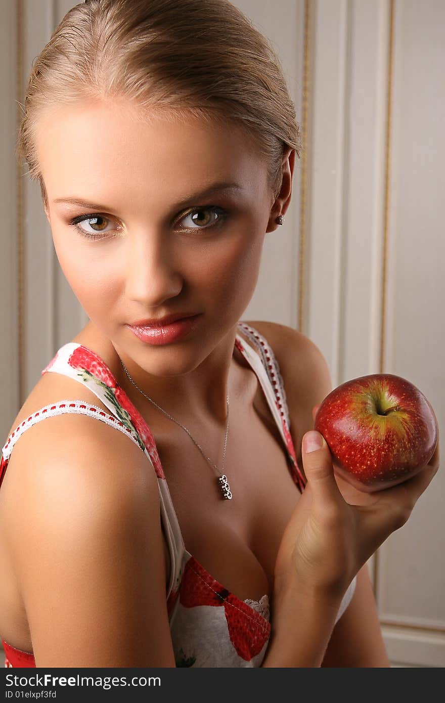 Portrait of attractive young woman holding red apple and looking at camera