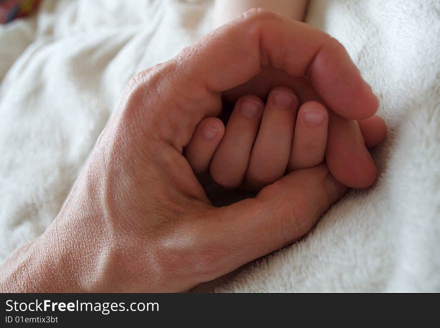 Mother holding her baby's little hand inside of hers, on a blanket. Mother holding her baby's little hand inside of hers, on a blanket.